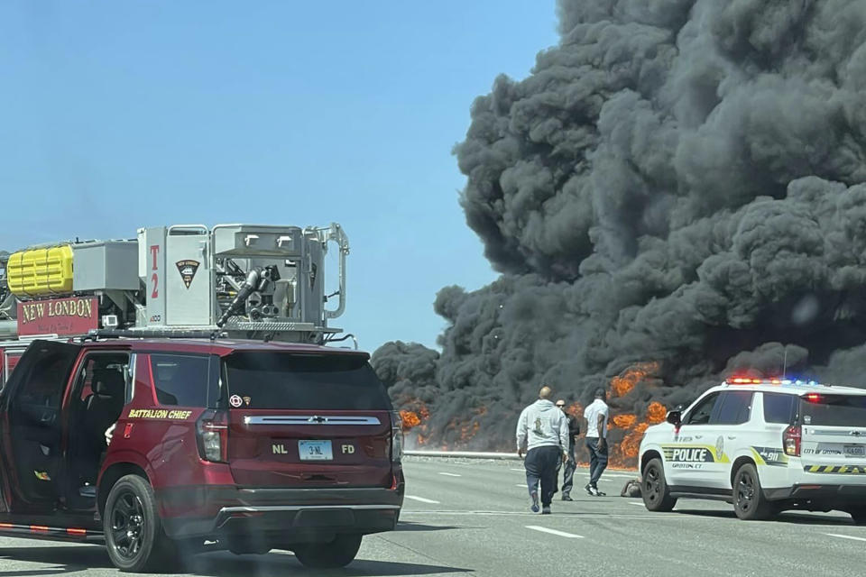 This photo provided by Angelique Feliciano shows firefighters and police responding after a crash involving a fuel truck and a car sparked a fire on the Gold Star Bridge between New London and Groton, Conn., on Friday, April 21, 2023. The crash closed Interstate 95 in both directions during the blaze. (Angelique Feliciano via AP)