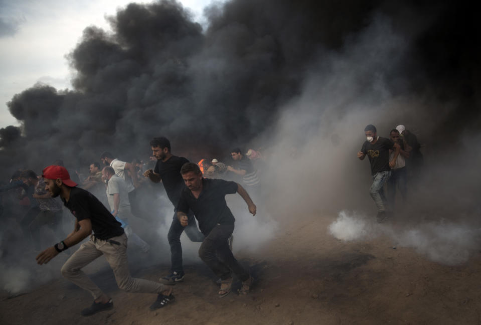 Palestinians run for cover from teargas fired from Israeli troops during a protest at the Gaza Strip's border with Israel, Friday, Oct. 5, 2018. (AP Photo/Khalil Hamra)