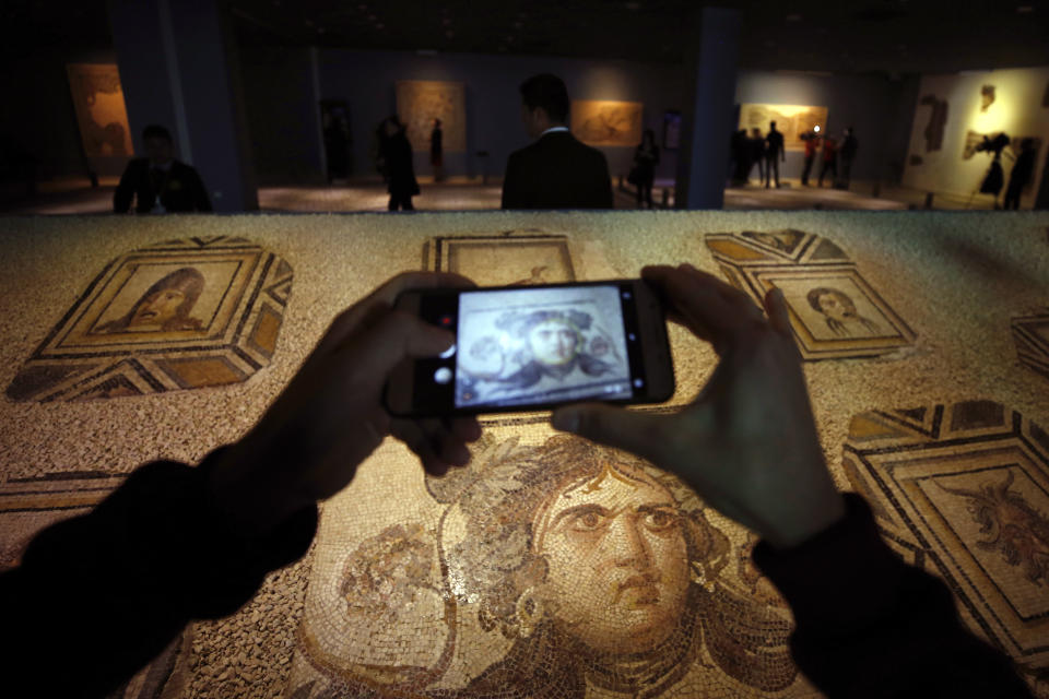 A visitor takes photos of Roman-era mosaics that were part of a U.S. university's art collection and were returned to Turkey, more than half a century after looters smuggled them out, during an exhibition at the Zeugma Mosaic Museum, in Gaziantep, Turkey, Saturday, Dec. 8, 2018. Ohio's Bowling Green State University bought the 12 mosaics from a New York gallery in 1965. Turkish and Bowling Green officials agreed to their return in May 2018. (AP Photo/Emrah Gurel)