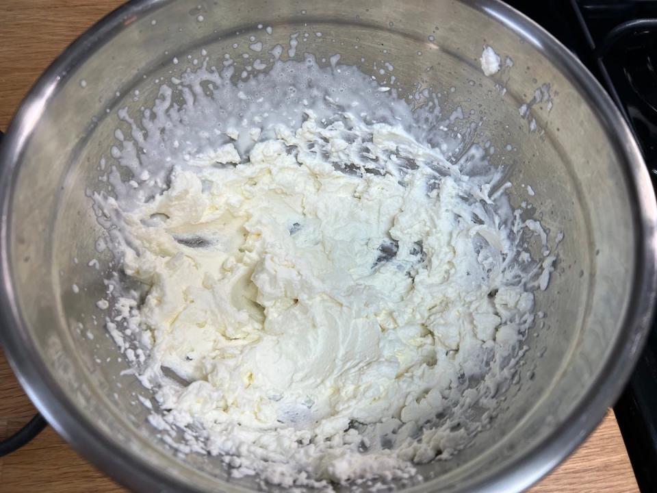 An overhead view of a silver mixing bowl with heavy whipping cream and confectioner's sugar, mixed until peaks form.