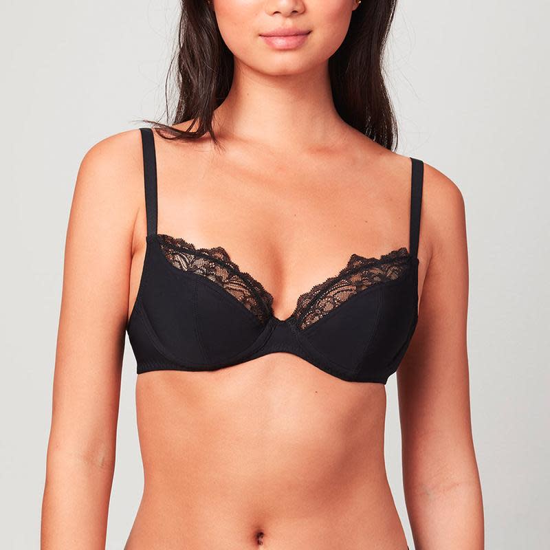 Model wearing a black Liberté Crosby Plunge Bra with Crosby performance micro jersey on the bottom cup and lace with scalloped edges on the top cup.