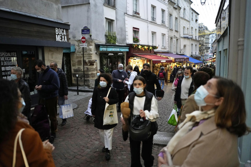 Pedestrians, some wearing protective face masks to prevent the spread of the COVID-19, walk in street market, in Paris, France, Friday, Dec. 31, 2021. Paris region health authorities have instructed hospitals to cancel more non-urgent medical procedures to free up intensive-care beds for the growing influx of people gravely sick with COVID-19. (AP Photo/Thibault Camus)