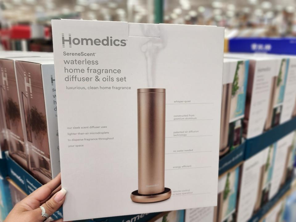 Hand holding a box of the Homedics home fragrance diffuser, which depicts a metal diffuser