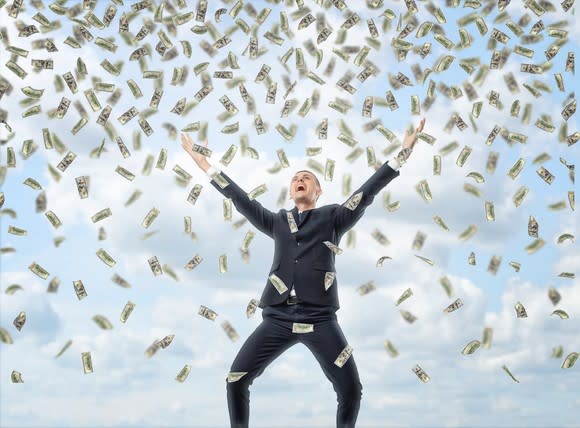 Cash raining down on a man standing with his arms up towards the sky.