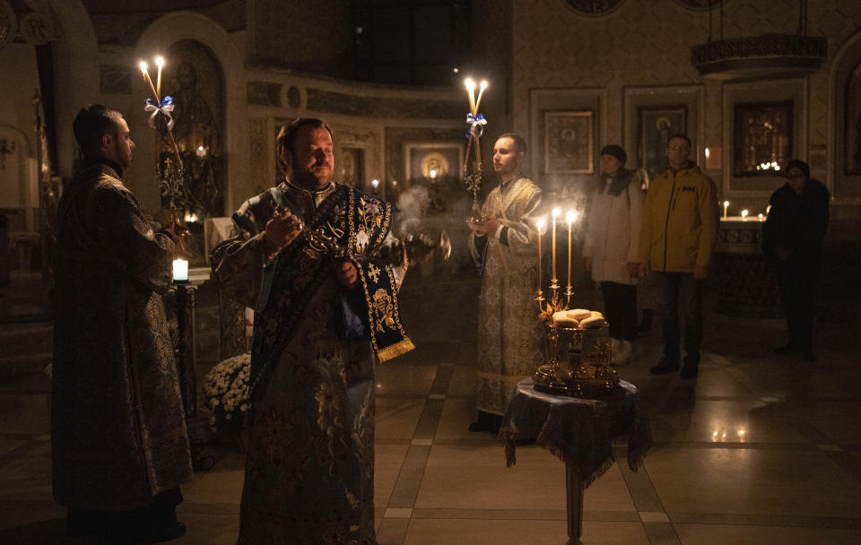 Priests deliver a religious service inside the Transfiguration of Jesus Orthodox Cathedral during blackout caused by recent Russian rocket attacks, in Kyiv, Ukraine, Saturday, Dec. 3, 2022. A top Orthodox priest in Ukraine's capital says he supports the efforts of President Volodymyr Zelenskyy's government and counter-intelligence agency to end Russian spying and meddling in Ukrainian politics through a Moscow-affiliated church. (AP Photo/Efrem Lukatsky)