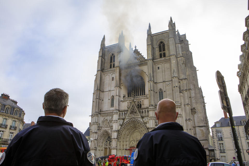 French police officers look at the blaze at the Gothic St. Peter and St. Paul Cathedral, in Nantes, western France, Saturday, July 18, 2020. The fire broke, shattering stained glass windows and sending black smoke spewing from between its two towers of the 15th century, which also suffered a serious fire in 1972. The fire is bringing back memories of the devastating blaze in Notre Dame Cathedral in Paris last year that destroyed its roof and collapsed its spire and threatened to topple the medieval monument. (AP Photo/Laetitia Notarianni)