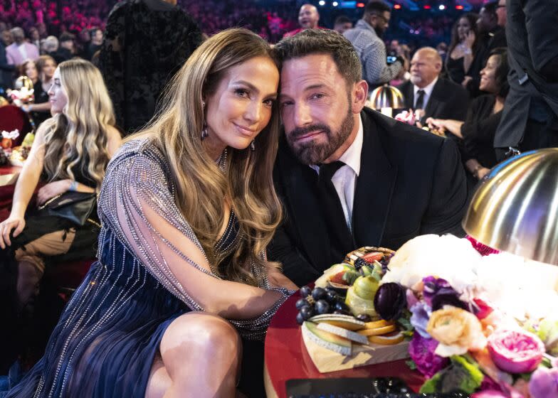 A woman and man in formalwear lean their heads together while sitting at a table with florals on it