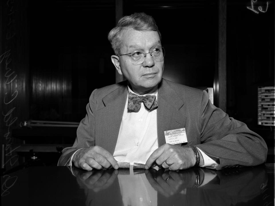 Nobel Prize winner Harold Urey wearing a bow tie and holding a fossil while sitting at a desk in 1951