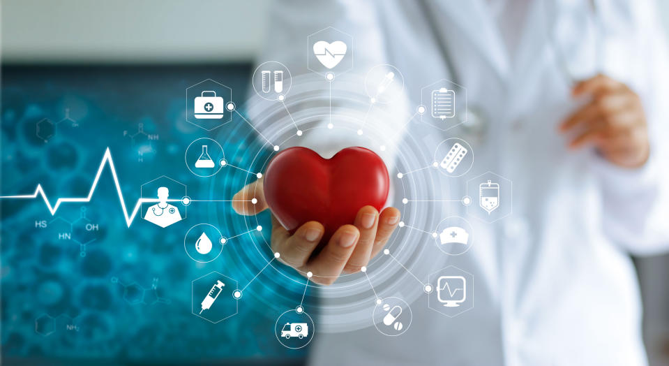 A person in a white lab coat holding out a stylized red heart with some digital icons surrounding it