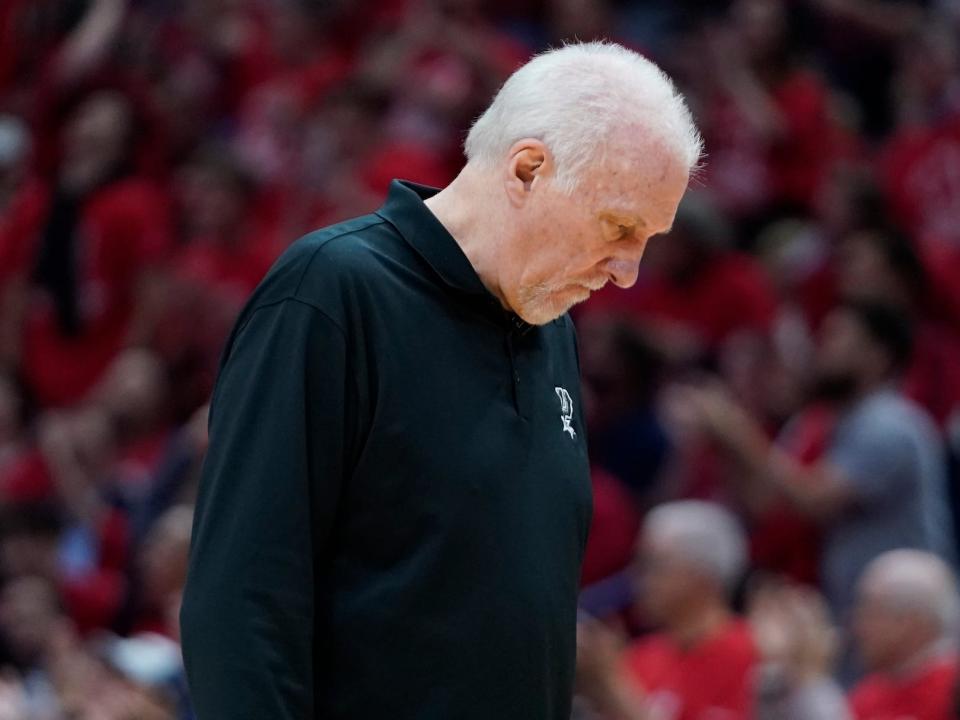 Gregg Popovich walks with his head down on the sidelines of a game.