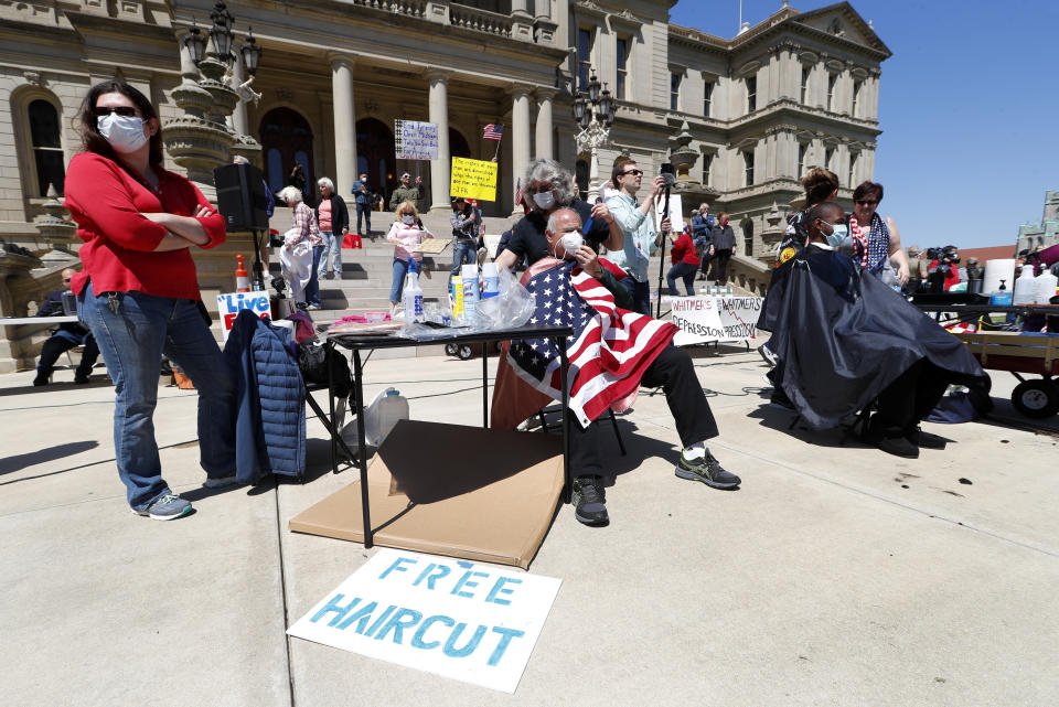 Annette Rafacz gives Manny Orovcoa a free haircut at the State Capitol during a rally in Lansing, Mich., Wednesday, May 20, 2020. Barbers and hair stylists are protesting the state's stay-at-home orders, a defiant demonstration that reflects how salons have become a symbol for small businesses that are eager to reopen two months after the COVID-19 pandemic began. (AP Photo/Paul Sancya)