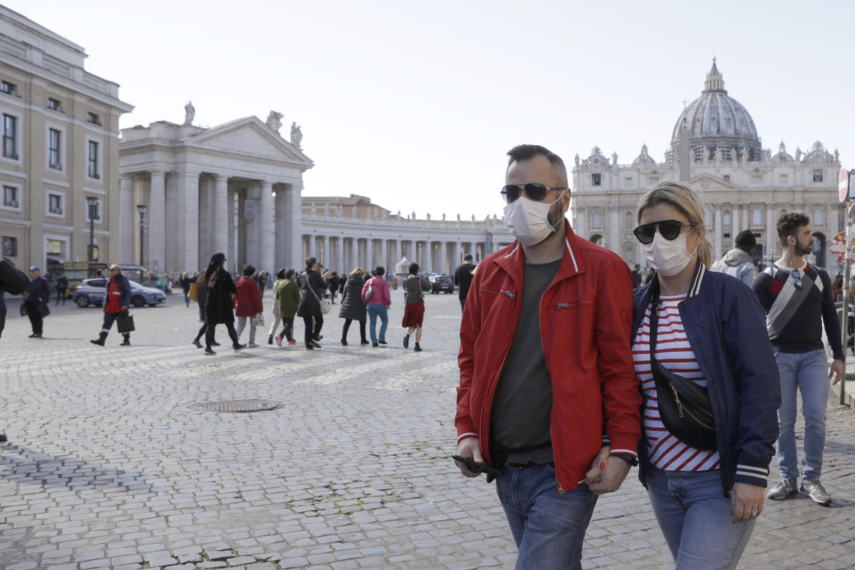 A couple wearing face masks, stroll outside St. Peter's Square, at the Vatican, Thursday, Feb. 27, 2020. In Europe, an expanding cluster in northern Italy is eyed as a source for transmissions of the COVID-19 disease (AP Photo/Gregorio Borgia)