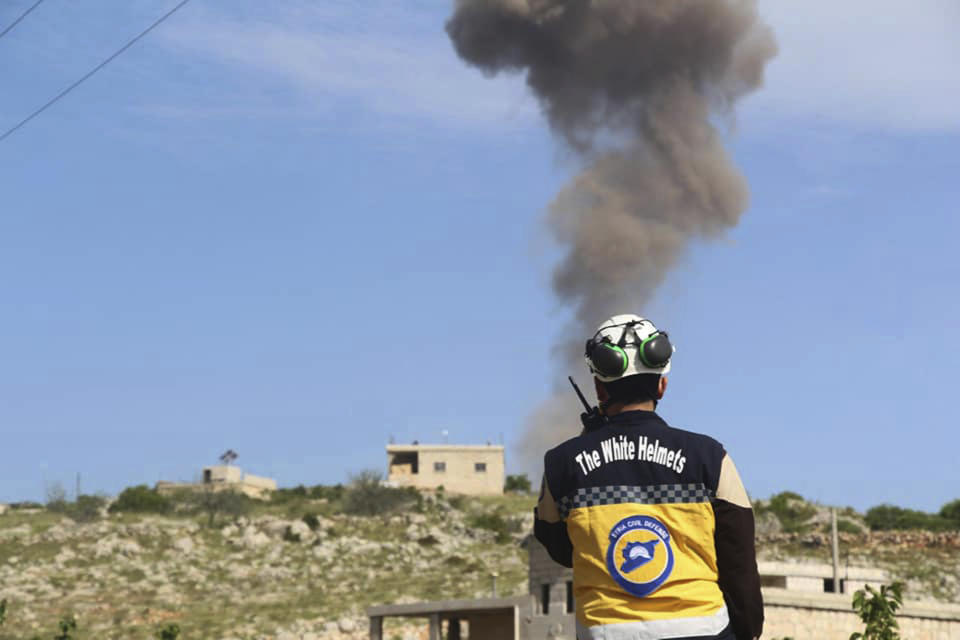 This photo provided by the Syrian Civil Defense White Helmets, which has been authenticated based on its contents and other AP reporting, shows a civil defense worker talks on his radio, as he looks to a smoke rises after Syrian government and Russian airstrikes hit the town of Ehssem, southern Idlib, Syria, Friday, May 3, 2019. Syrian state media and activists are reporting a wave of government and Russian airstrikes, including indiscriminate barrel bombs, on the rebel-held enclave in northwestern Syria where a seven-month truce is teetering under a violent escalation. (Syrian Civil Defense White Helmets via AP)