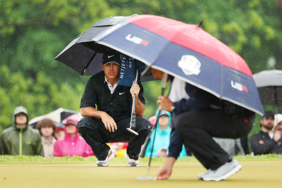 Brooks Koepka and Bryson DeChambeau hide under the umbrellas