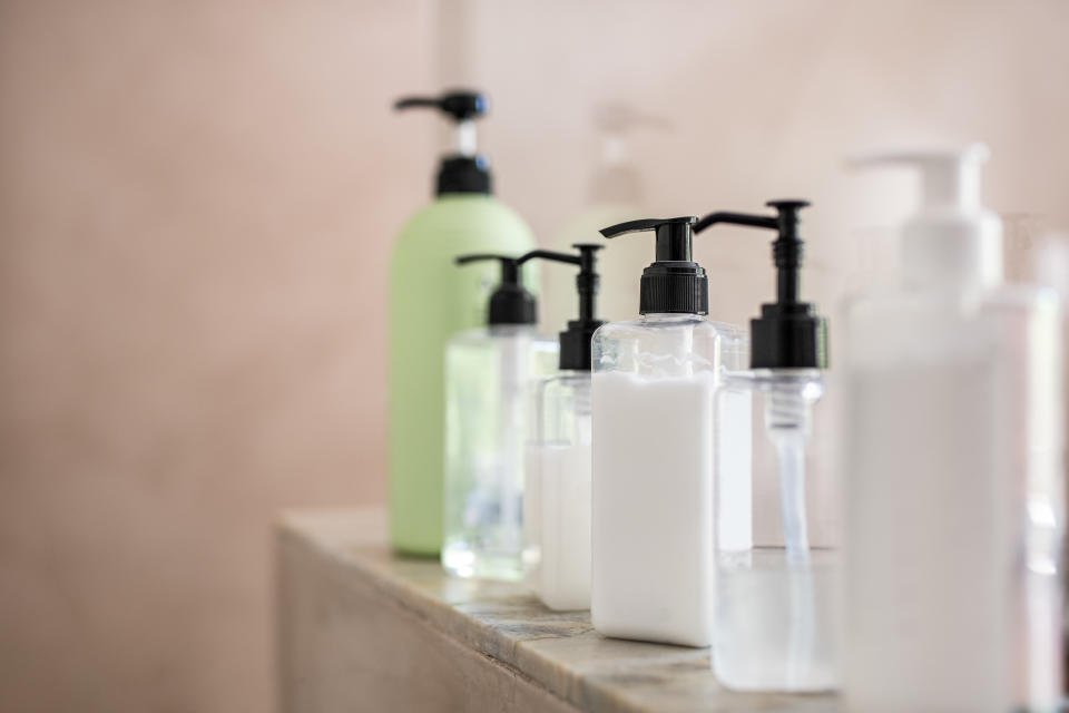 Dispenser bottles in a row kept on rack in bathroom. Close up of multiple shampoo, soap and body lotion bottles on marble at spa. Bottle of soap and liquid in bathroom.