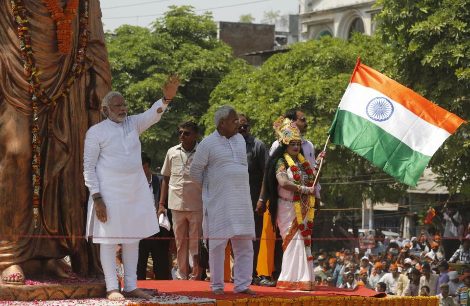 India's main opposition Bharatiya Janata Party's (BJP) Prime ministerial candidate Narendra Modi waves to supporters as a woman dressed as Mother india waves the national flag in Varanasi, in the northern Indian state of Uttar Pradesh, Thursday, April 24, 2014. During his campaign, Modi has not played up his party's Hindu agenda, but experts say his decision to run in this holy city is meant to send a clear message to all voters about his commitment to the BJP's brand of religious nationalism, which emphasizes India's Hindu identity. (AP Photo/Rajesh Kumar Singh)