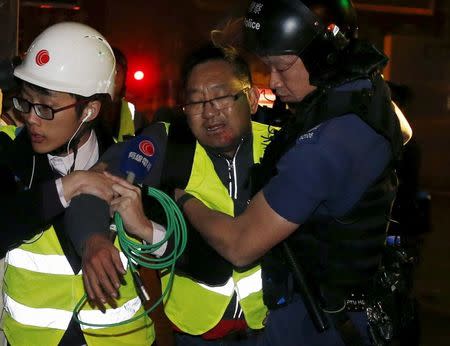 An injured TV journalist (C) is helped by his colleague and a riot policeman after being hit by a stone thrown by a protester onto his face during a clash at Mongkok district in Hong Kong, China February 9, 2016. REUTERS/Bobby Yip