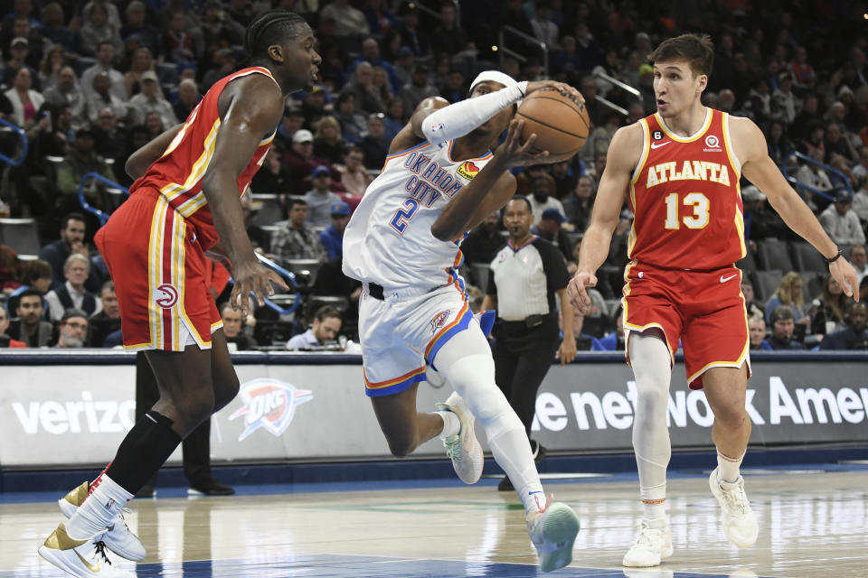 Oklahoma City Thunder guard Shai Gilgeous-Alexander, middle, pushes past Atlanta Hawks center Clint Capela, left, and forward Bogdan Bogdanovic, right in the second half of an NBA basketball game, Wednesday, Jan. 25, 2023, in Oklahoma City. (AP Photo/Kyle Phillips)