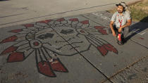 Native American advocate Carl Moore sits next to Native American imagery painted along a walkway which leads from the Bountiful High School parking lot up to the football field Tuesday, July 28, 2020, in Bountiful, Utah. While advocates have made strides in getting Native American symbols and names changed in sports, they say there's still work to do mainly at the high school level, where mascots like Braves, Indians, Warriors, Chiefs and Redskins persist. (AP Photo/Rick Bowmer)