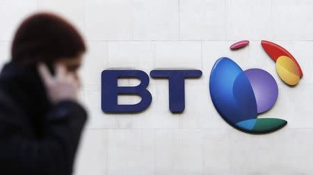 A man talks on his mobile telephone as he walks past a BT logo in London, February 5, 2015. REUTERS/Suzanne Plunkett