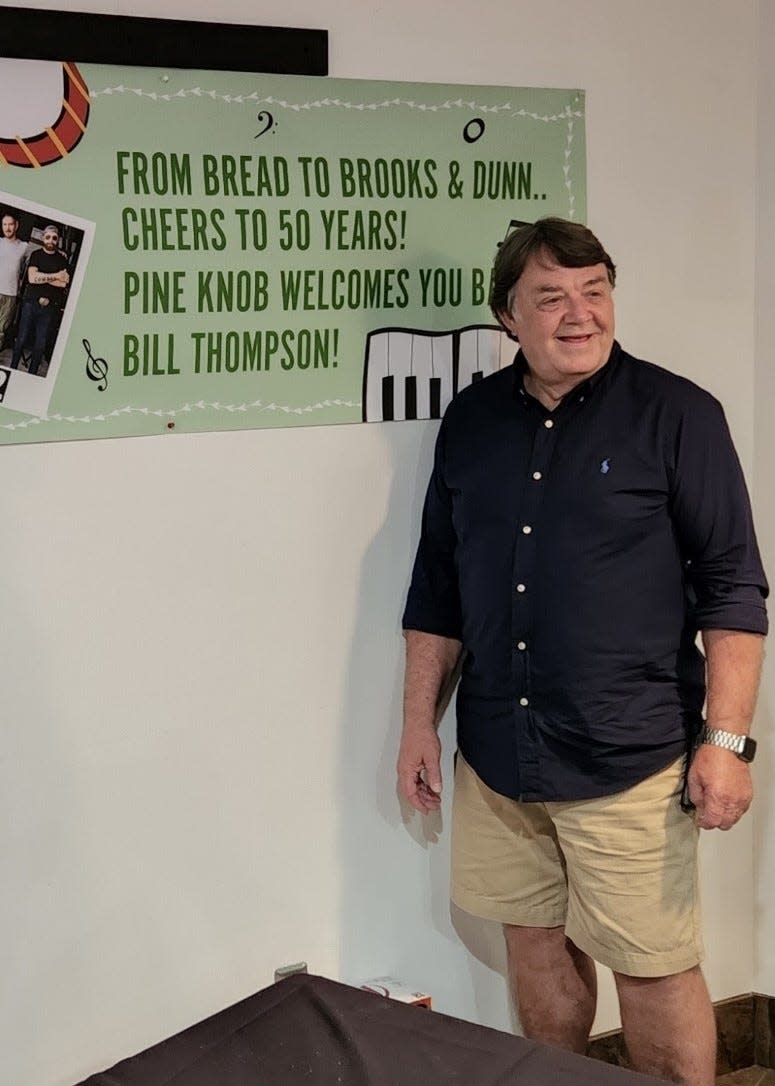 Bill Thompson, tour manager for country duo Brooks & Dunn, poses backstage at Pine Knob Music Theatre on June 25, 2022, with a banner commemorating his first-ever show at the venue in August 1972.