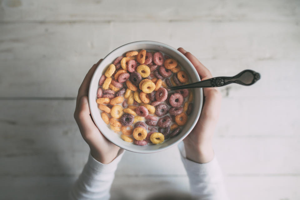 Little girl eating colorful ring-shaped cereal in a bowl of milk, seen from above, Lifestyle concept.