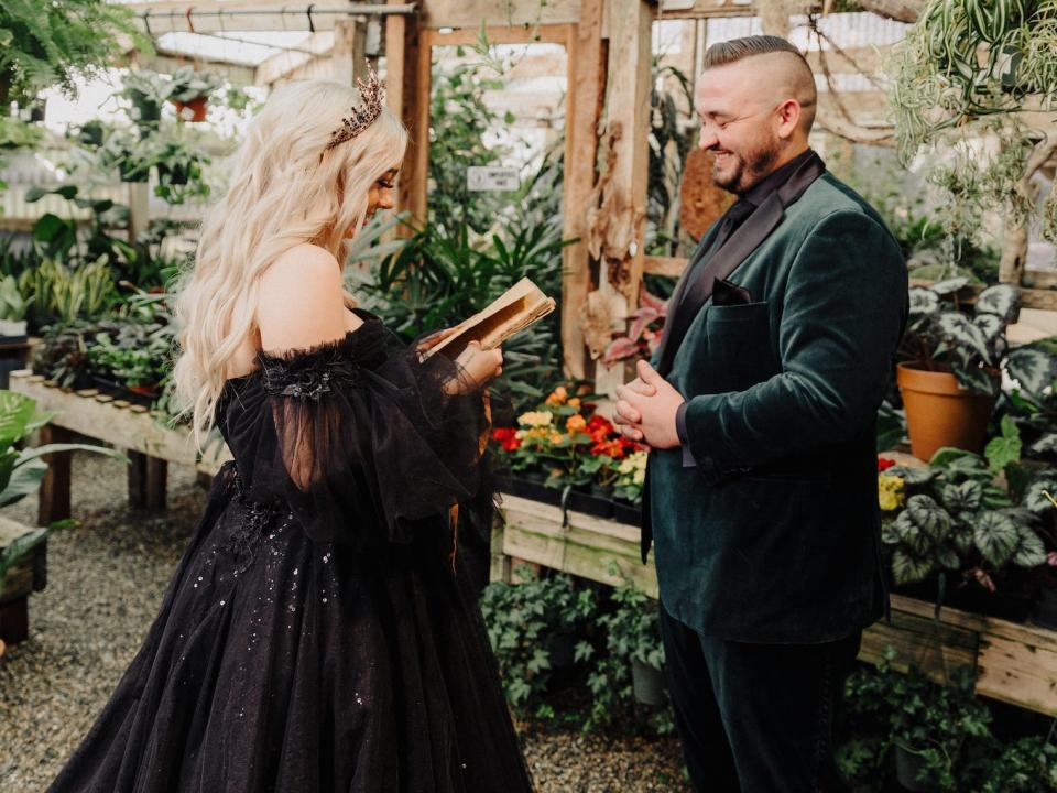 A bride and groom read vows to each other in a greenhouse.