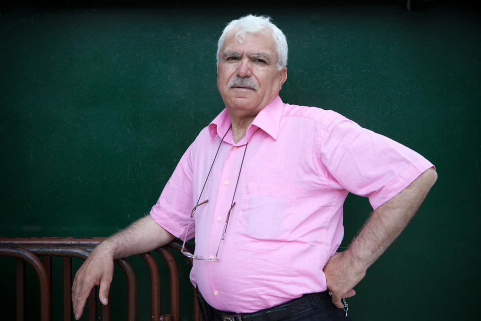 An older man wearing a pink dress shirt as he leans against a railing