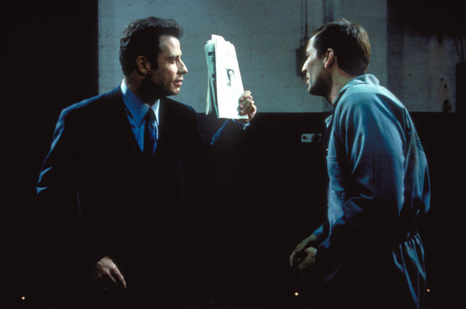 John Travolta holding up a file to Nicolas Cage.