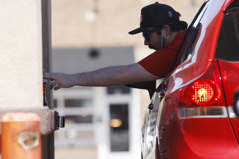 A motorist reaches to the jar to leave a tip for workers at a drive-thru window of a Dunkin Donuts as a stay-at-home order reamins in force for residents while still dealing with the dangers of the new coronavirus Tuesday, April 28, 2020, in Denver. (AP Photo/David Zalubowski)