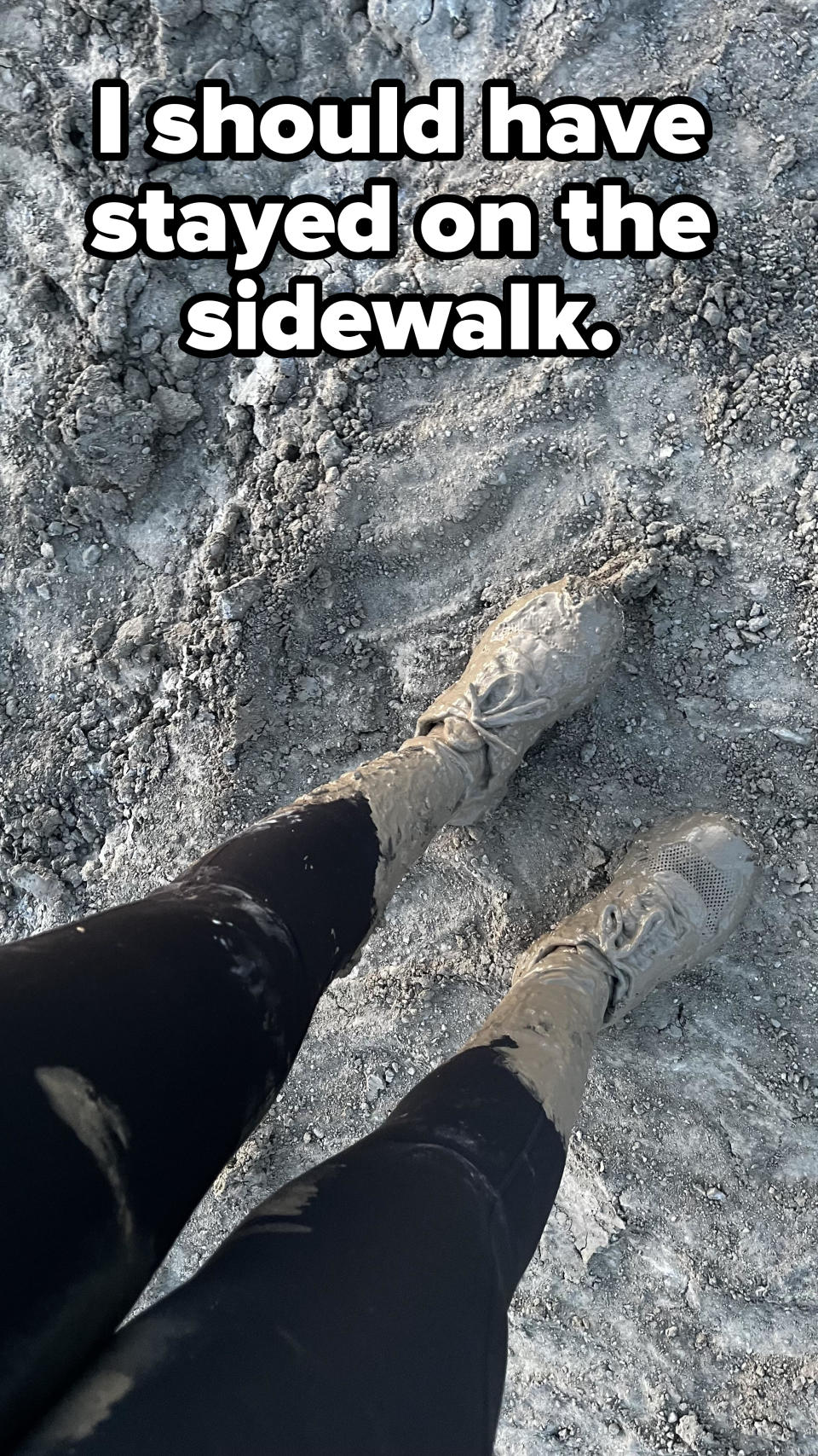 Person standing in muddy terrain with mud-covered boots and lower legs