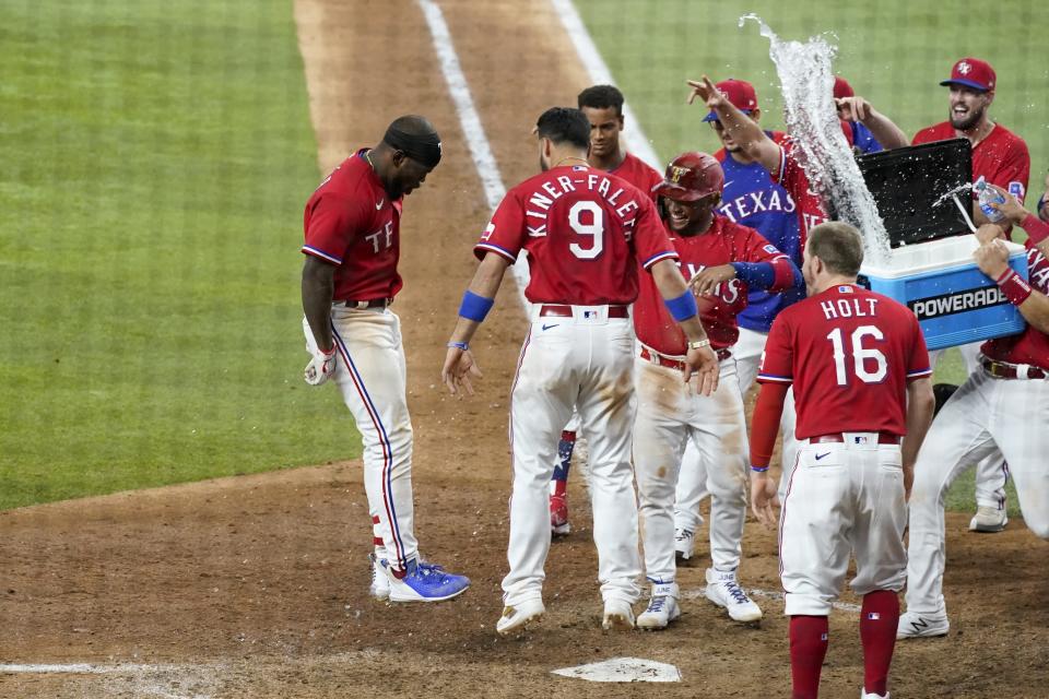 Texas Rangers' Adolis Garcia, left, leaps onto home plate celebrating with the team after hitting a three-run home run in the 10th inning of the team's baseball game against the Houston Astros in Arlington, Texas, Friday, May 21, 2021. (AP Photo/Tony Gutierrez)