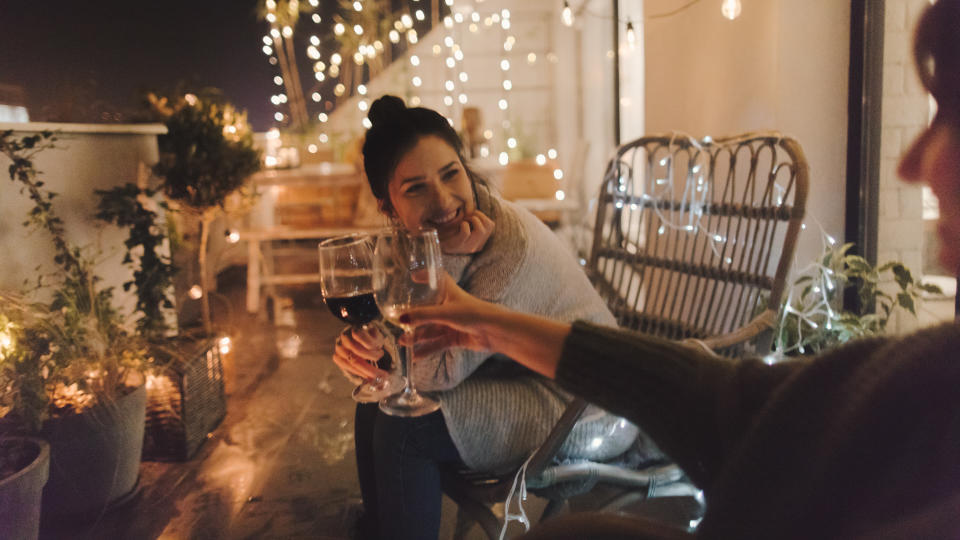 Young smiling woman enjoying in good wine and great company on the open terrace of her loft apartment.