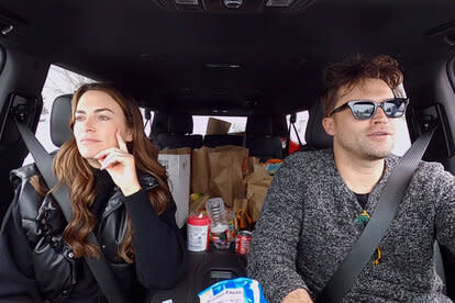 Tom Schwartz driving a car and Katie Flood in the passenger seat.