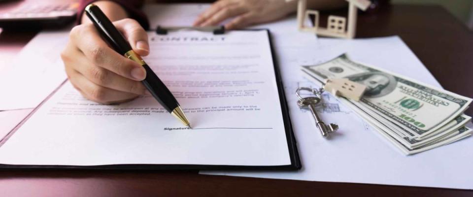 Real Estate Agent's Hand pointing signature Client in Contract Form on table with money, purchase agreement, house key, design home document.