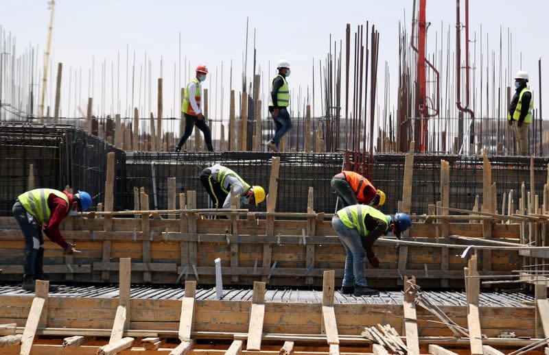 Workers wearing protective face masks stand on a building under construction in the New Administrative Capital (NAC), east of Cairo