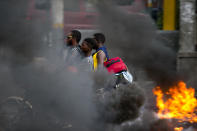 FILE - In this Sept. 17, 2019 file photo, a moto-taxi driver takes two passengers past a burning barricade during a protest against fuel shortages in Port-au-Prince, Haiti. Haiti's economy, already fragile when the new round of protests began in mid-Sept., is in deep trouble with spiraling inflation and dwindling supplies, including fuel. (AP Photo/Dieu Nalio Chery, File)