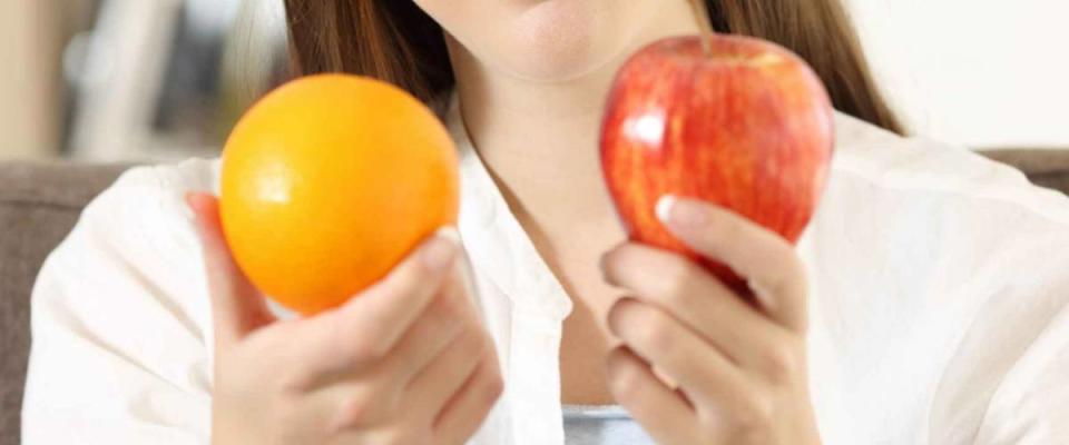 Girl deciding between two fruits an apple and an orange sitting on a couch in the living room at home