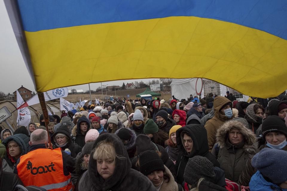 FILE - Ukrainian volunteer Oleksandr Osetynskyi, 44 holds a Ukrainian flag and directs hundreds of refugees after fleeing from the Ukraine and arriving at the border crossing in Medyka, Poland, Monday, March 7, 2022. Nearly a year has passed since the Feb. 24, 2022, invasion sent millions of people fleeing across Ukraine's border into neighboring Poland, Slovakia, Hungary, Moldova and Romania. (AP Photo/Visar Kryeziu, File)