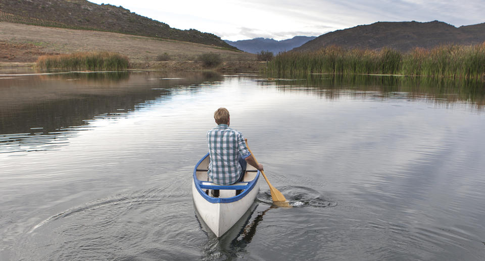 A man canoeing on a lake in Malawi with his back to the camera.