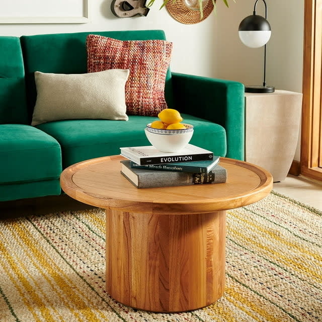 a natural brown pedestal coffee table in a living room with a green couch