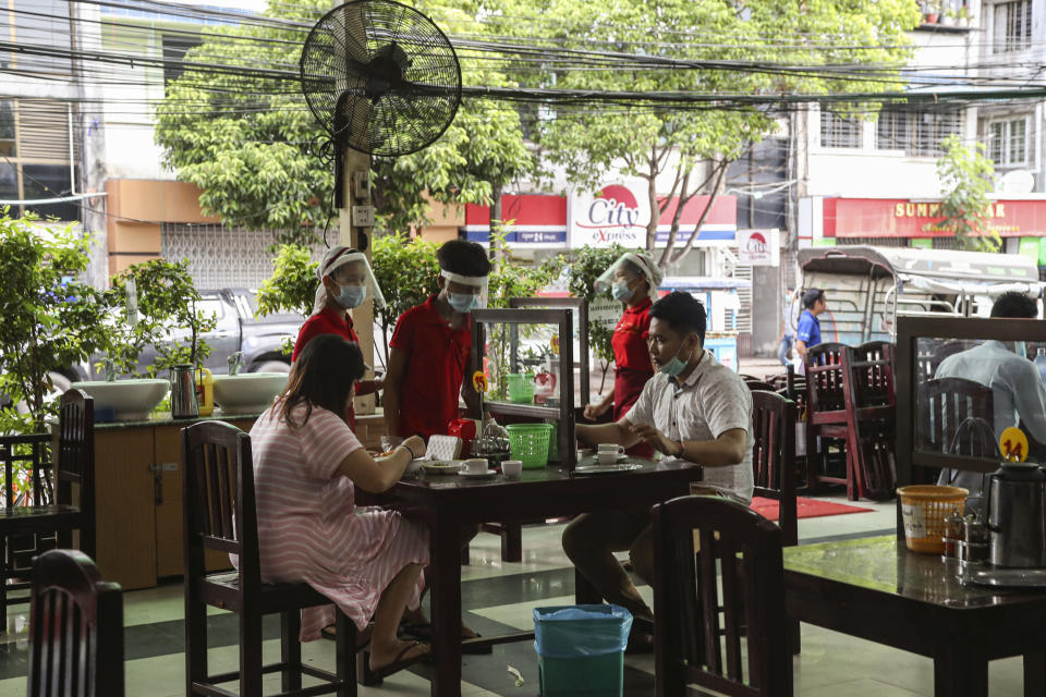 A waiter with a face shield serves foods to customers sitting behind mirror aluminum frame to help curb the spread of the new coronavirus at a tea-shop in Yangon, Myanmar Monday, May 18, 2020. (AP Photo/Thein Zaw)