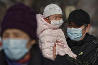 A man carries a child, both wearing face masks to help curb the spread of the coronavirus, as they stroll along a street near the popular frozen Houhai Lake in Beijing, Thursday, Jan. 21, 2021. China is making some of its toughest travel restrictions yet as coronavirus cases surge in several northern provinces ahead of the travel rush for Lunar New Year on next month. (AP Photo/Andy Wong)