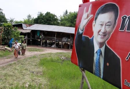 Villagers walk past a poster of ousted former Thai Prime Minister Thaksin Shinawatra in a village in Sakon Nakhon province May 26, 2011. REUTERS/Sukree Sukplang/Files