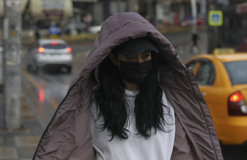 A woman wearing a mask to help protect against the spread of coronavirus, walk in the rain in Ankara, Turkey, Monday, March 29, 2021. Turkey is reinstating weekend lockdowns in most of Turkey's provinces and will also impose restrictions over the Muslim holy month of Ramadan following a sharp increase in COVID-19 cases.(AP Photo/Burhan Ozbilici)