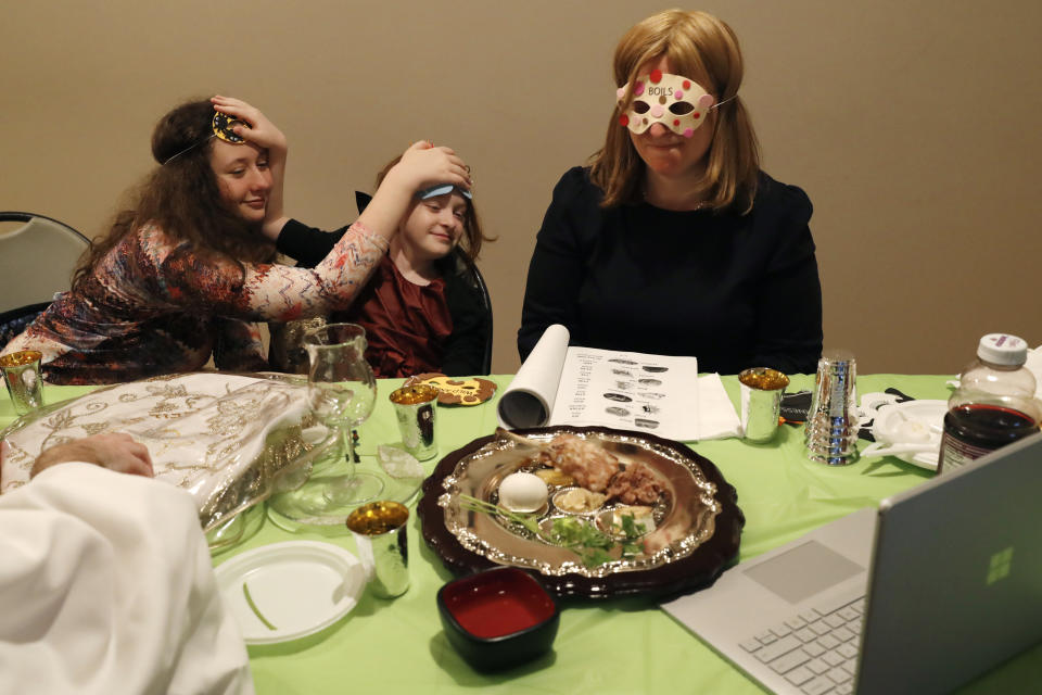 Wearing masks depicting some ten plagues inflicted on Egyptians during ancient times, Shira Segal, left, and younger sister Rayna, 8, center, clown around in front of a laptop computer broadcasting their Passover seder, as their mother Adina, right, dons a mask representing "boils," during the servie for members of their congregation, friends and family, from their home in the Sheepshead Bay section of Brooklyn during the current coronavirus outbreak, Wednesday, April 8, 2020, in New York. With the deadly COVID-19 virus in full swing in New York and around the country, the reading of the plagues is particularly resonant this year. According to the story, after Pharaoh refused Moses' pleas to let enslaved Israelites go free, God sent a series of ten plagues to pressure the Egyptian ruler. Each time Pharaoh promises to free the Israelites, but reverses his decision when the plague is lifted, until the last one. The plagues are: water turning to blood, frogs, lice, flies, livestock pestilence, boils, hail, locusts, darkness and the killing of first-born children. Passover commemorates the Israelites' freedom from slavery in ancient Egypt in the wake of the ten plagues. (AP Photo/Kathy Willens)