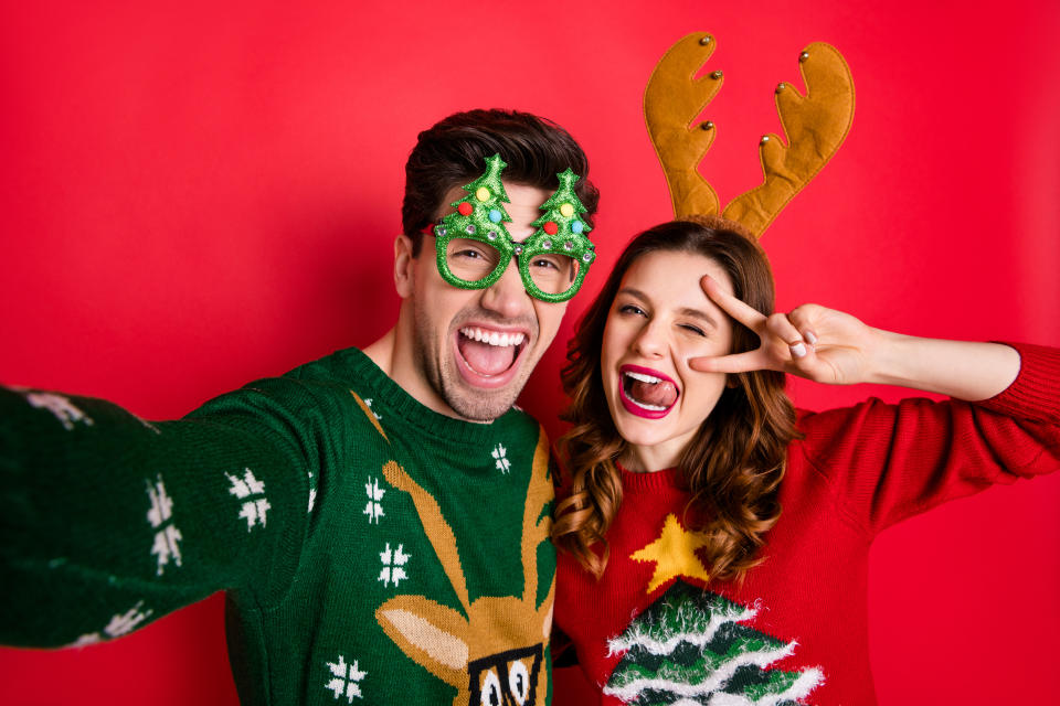 Photo of crazy couple making selfies sticking tongues winking eyes v-signing, wear funky ugly ornaments jumpers isolated red color background