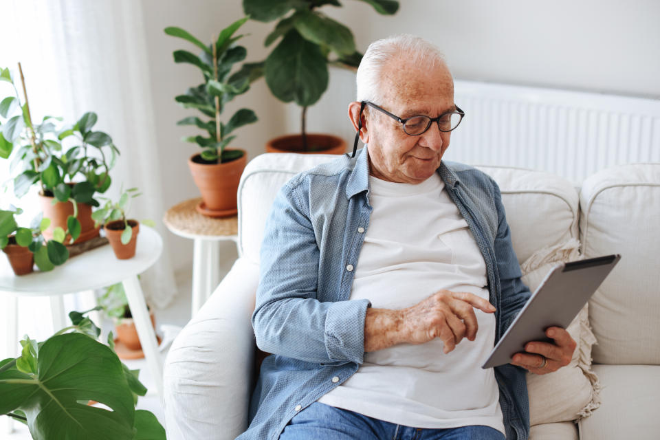 Happy senior man uses digital tablet while in his home