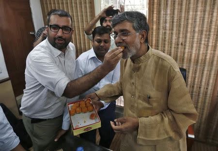 Children's right activist Kailash Satyarthi (R) is offered sweets by a well-wisher at his office in New Delhi October 10, 2014. REUTERS/Adnan Abidi