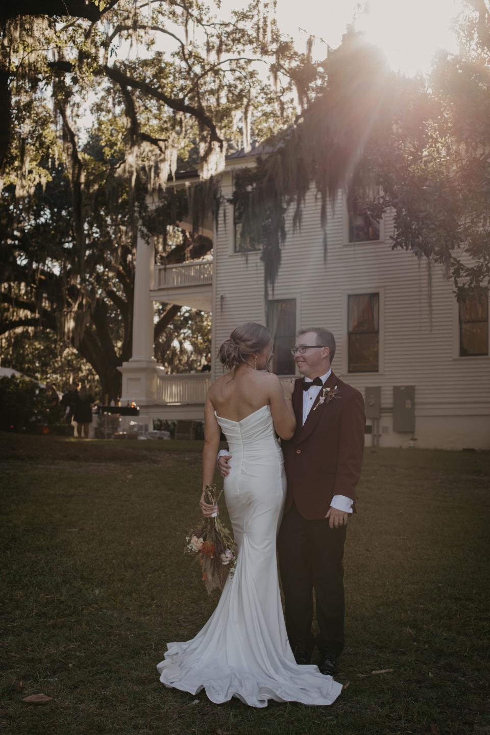 A bride looks at her groom as he smiles at her in front of a house.